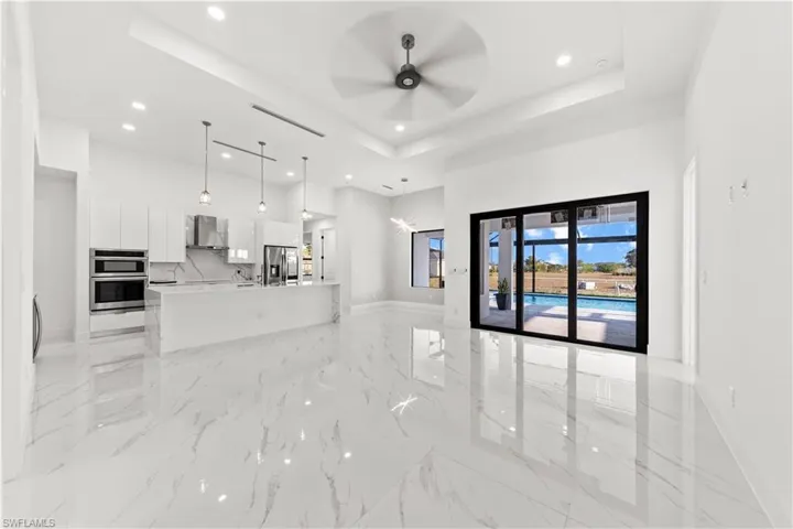 Unfurnished living room with a tray ceiling, a high ceiling, marble finish floor, ceiling fan, and recessed lighting