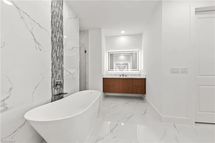 Bathroom featuring vanity, a soaking tub, walk in shower, marble finish floor, and recessed lighting