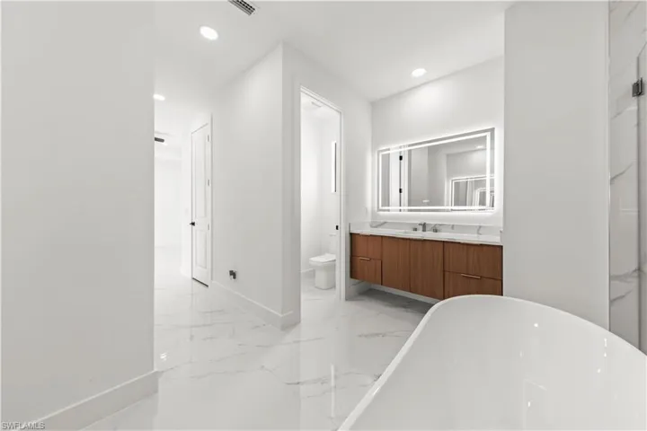 Full bath featuring marble finish floor, recessed lighting, a soaking tub, and vanity