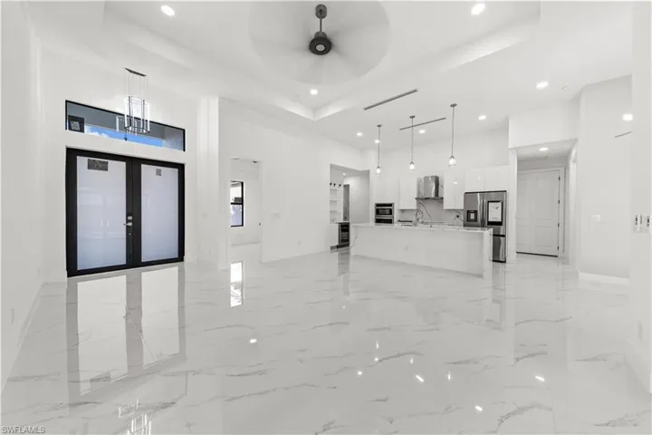 Unfurnished living room featuring a tray ceiling, a ceiling fan, a high ceiling, marble finish floor, and recessed lighting