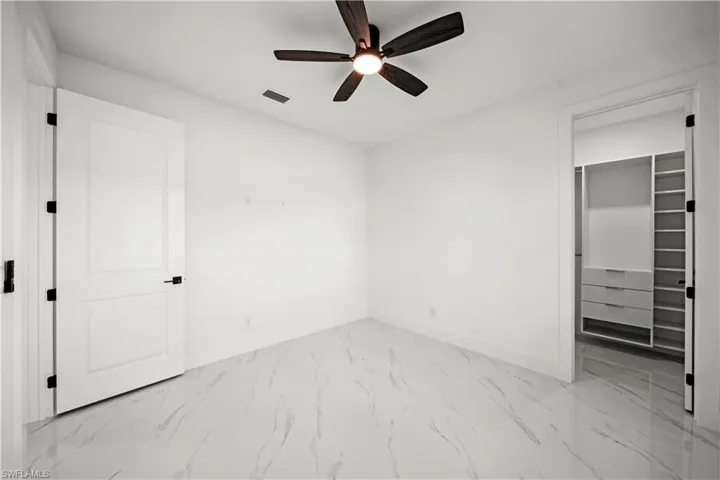 Unfurnished bedroom featuring a ceiling fan, a walk in closet, marble finish floor, baseboards, and visible vents