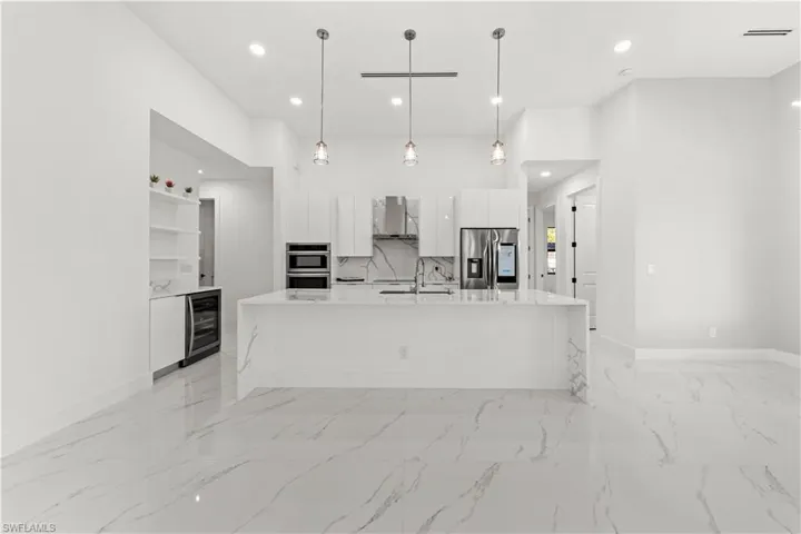 Kitchen featuring white cabinets, modern cabinets, wall chimney exhaust hood, stainless steel appliances, and beverage cooler