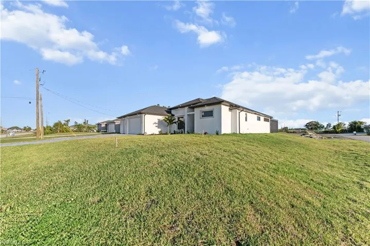 View of front of house with a front yard, stucco siding, an attached garage, and driveway