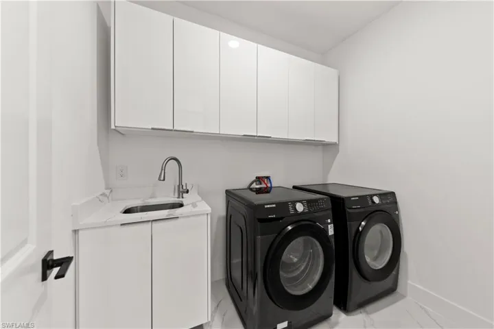 Washroom featuring marble finish floor, washer and dryer, cabinet space, and a sink