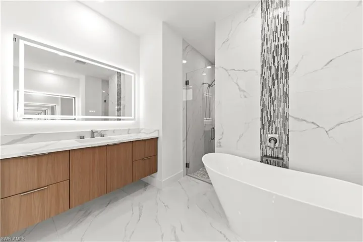 Bathroom featuring visible vents, a soaking tub, marble finish floor, a marble finish shower, and vanity