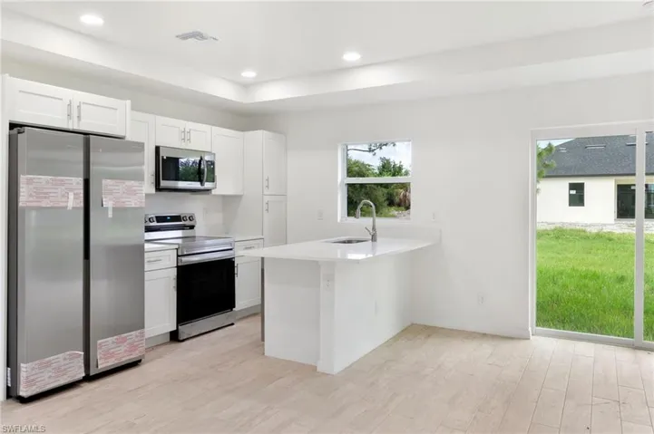 Kitchen with light hardwood / wood-style flooring, white cabinets, appliances with stainless steel finishes, and sink