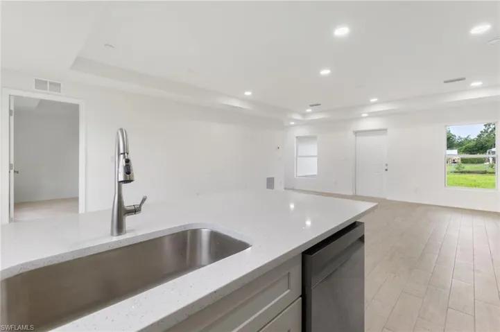 Kitchen with light stone counters, sink, stainless steel dishwasher, a tray ceiling, and light hardwood / wood-style floors