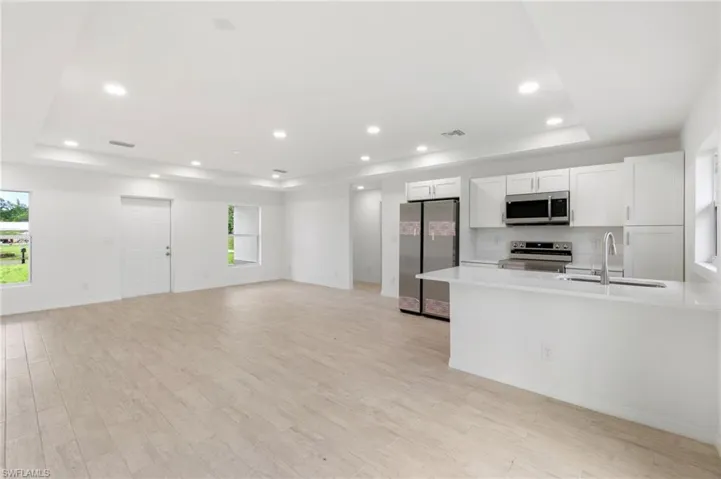 Kitchen featuring white cabinets, sink, light hardwood / wood-style flooring, a tray ceiling, and stainless steel appliances