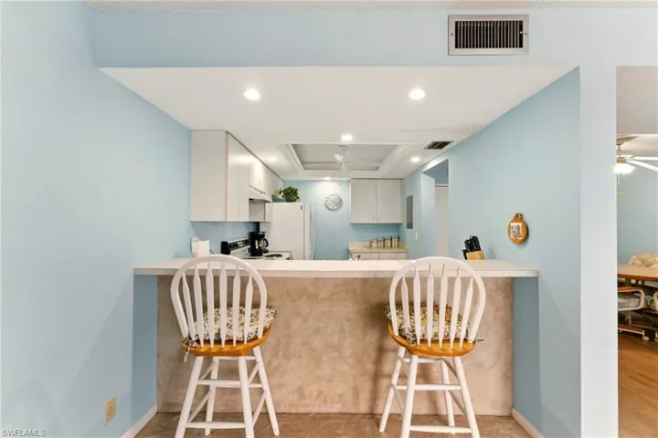 Kitchen with a breakfast bar, light countertops, recessed lighting, white cabinetry, and a tray ceiling