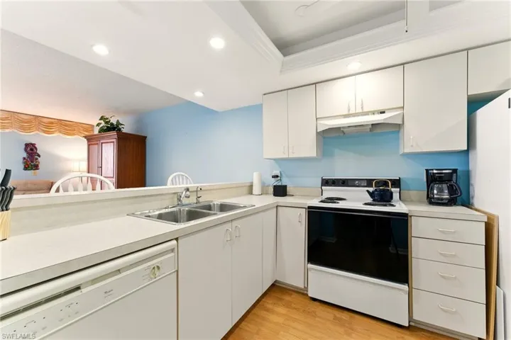 Kitchen with white appliances, light countertops, light wood-style flooring, white cabinets, and recessed lighting