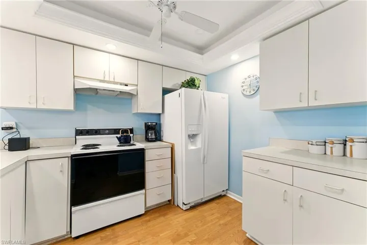 Kitchen with white appliances, light countertops, light wood finished floors, recessed lighting, and white cabinets