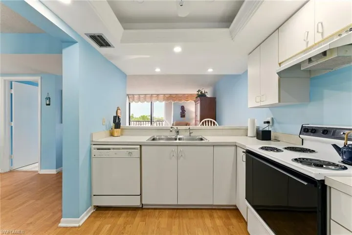 Kitchen with electric stove, white cabinets, white dishwasher, light countertops, and recessed lighting