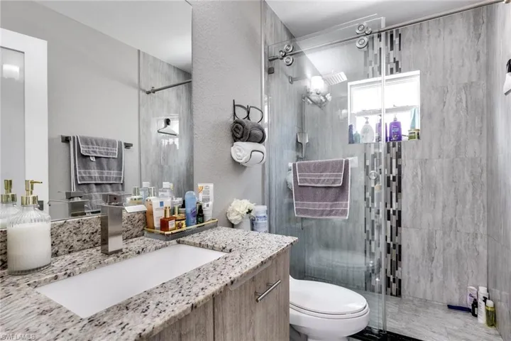Full bathroom featuring a textured wall, vanity, toilet, and a stall shower