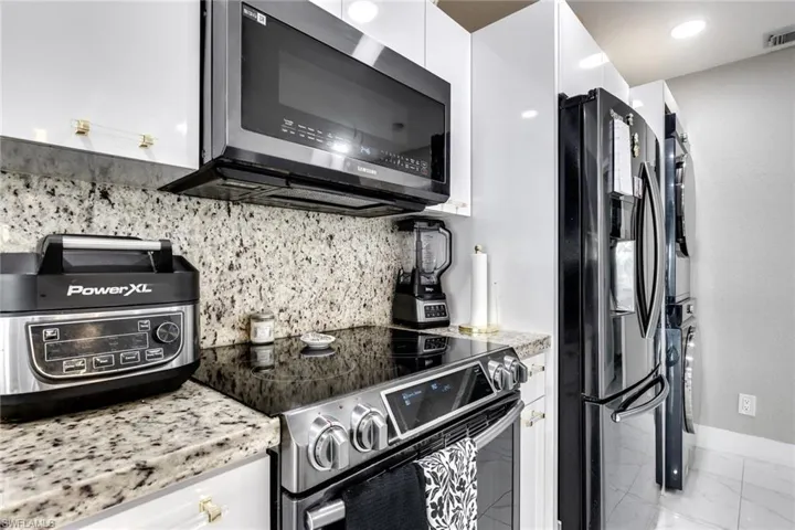 Kitchen featuring backsplash, marble finish floor, white cabinetry, and appliances with stainless steel finishes