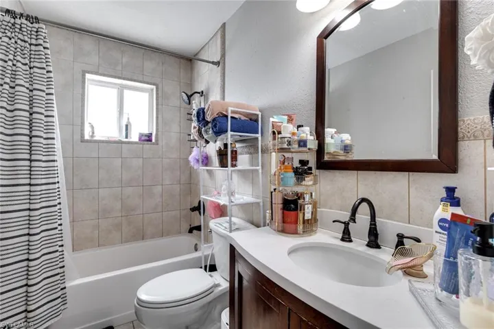 Bathroom featuring tile walls, shower / bath combo with shower curtain, toilet, and vanity