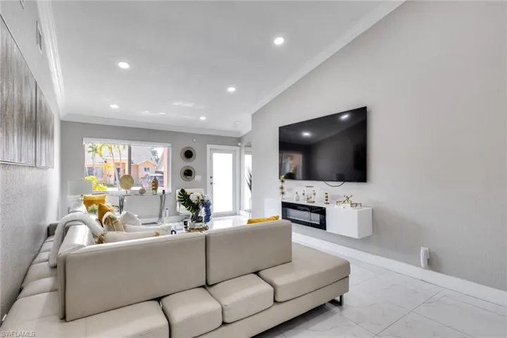 Living area with baseboards, a glass covered fireplace, recessed lighting, marble finish floor, and ornamental molding