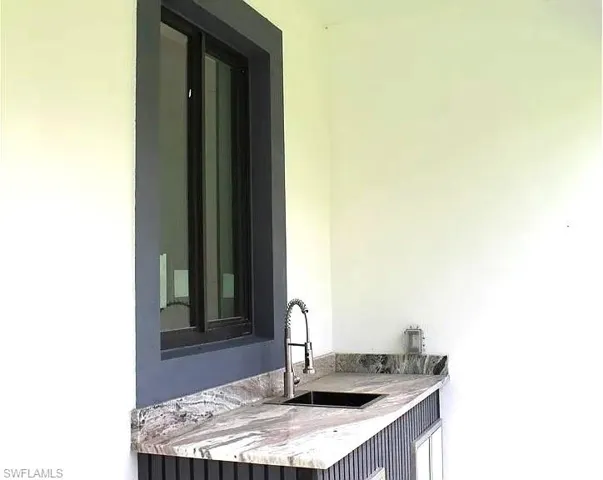 Outdoor wet bar featuring a stone countertop, built-in sink, and pull-down faucet