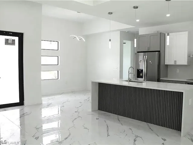 Modern kitchen featuring a waterfall island with fluted paneling, a stainless steel refrigerator, contemporary pendant lighting, and white cabinetry
