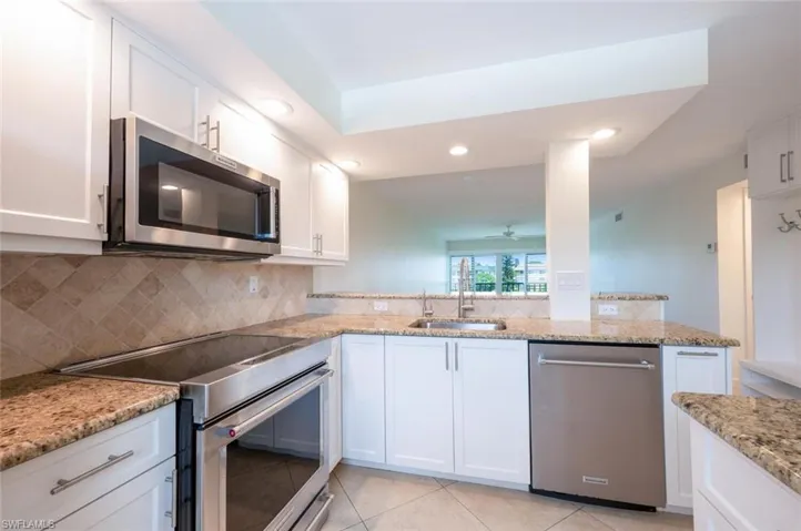 Kitchen featuring stainless steel appliances, white cabinetry, light stone countertops, light tile patterned floors, and recessed lighting