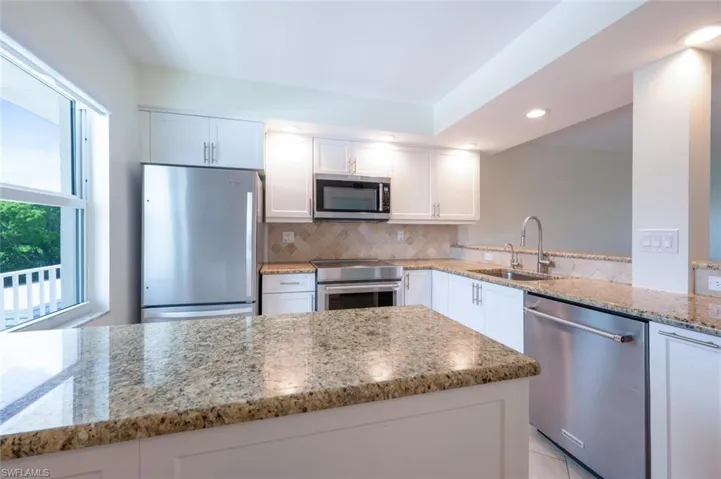 Kitchen featuring appliances with stainless steel finishes, white cabinets, light stone countertops, decorative backsplash, and recessed lighting
