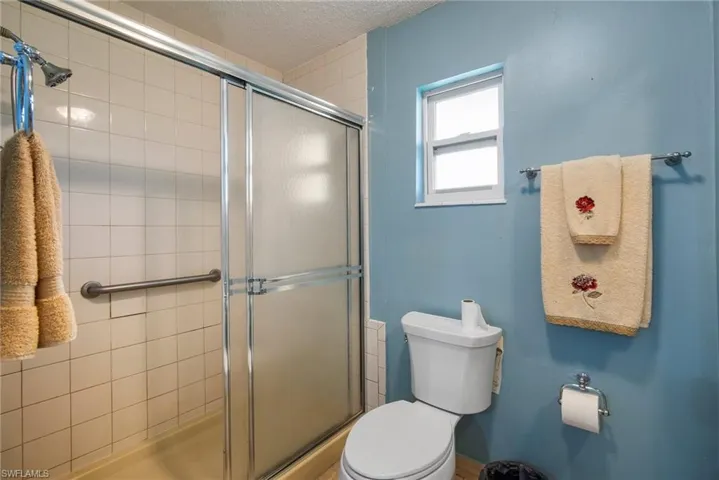 Bathroom featuring toilet, a textured ceiling, and a shower with door