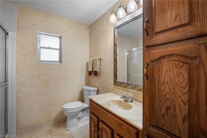 Bathroom featuring tile patterned flooring, a textured ceiling, vanity, an enclosed shower, and toilet