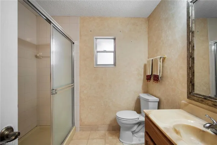 Bathroom with toilet, a textured ceiling, tile patterned flooring, and walk in shower