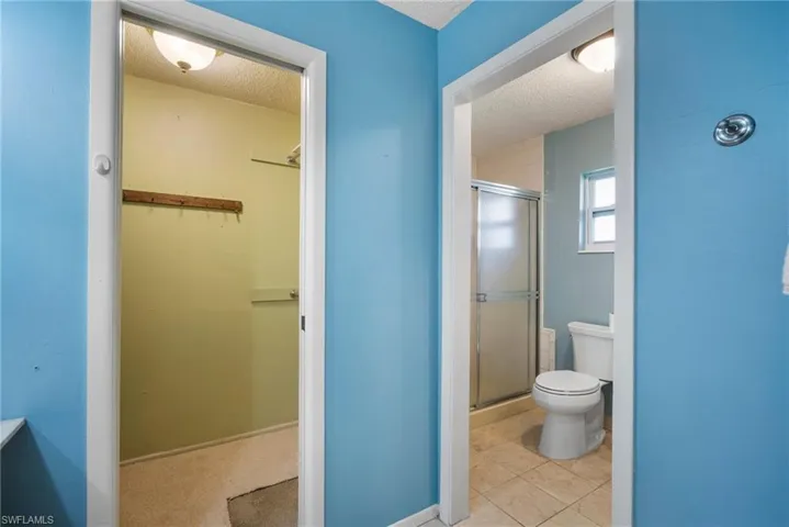 Bathroom featuring toilet, a textured ceiling, tile patterned flooring, and a shower with shower door