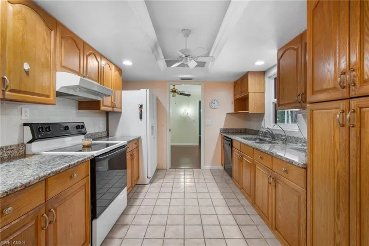 Kitchen featuring sink, light stone counters, ceiling fan, white range with electric cooktop, and dishwasher