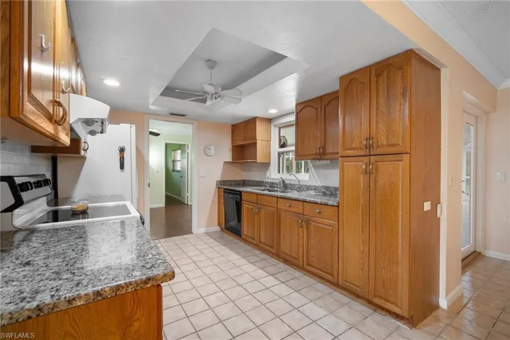 Kitchen with stone countertops, sink, a tray ceiling, range, and dishwasher