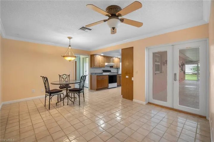 Tiled dining room with ornamental molding, french doors, ceiling fan, and a textured ceiling