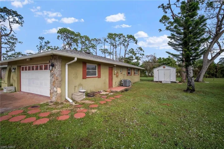 View of property exterior with central AC unit, a garage, a yard, and a storage shed