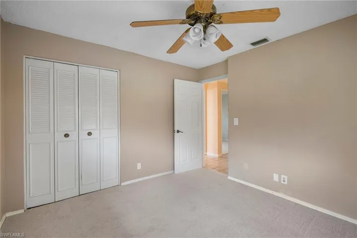 Unfurnished bedroom featuring a closet, a textured ceiling, light carpet, and ceiling fan