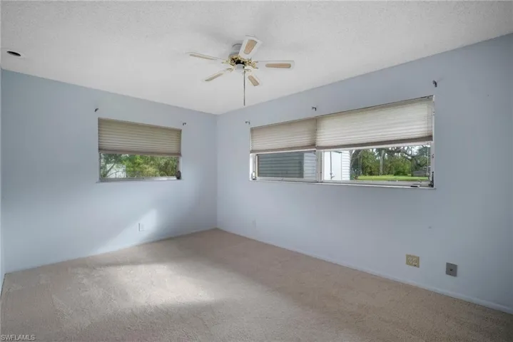Carpeted empty room with a textured ceiling, ceiling fan, and plenty of natural light