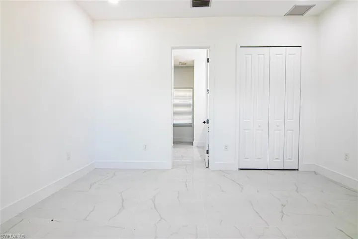 Unfurnished bedroom with ensuite bathroom, light marble finish floors, and a closet