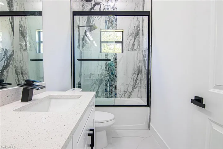 Full bathroom featuring vanity, bath / shower combo with glass door, and light marble finish floors