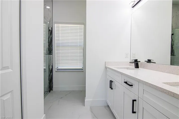 Bathroom with double vanity, a marble finish shower, and light marble finish flooring