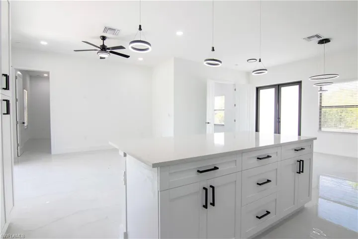 Kitchen with white cabinetry, hanging light fixtures, a kitchen island, light stone countertops, and a ceiling fan