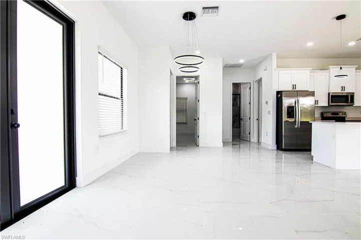 Kitchen with stainless steel appliances, white cabinets, hanging light fixtures, and light marble finish floors