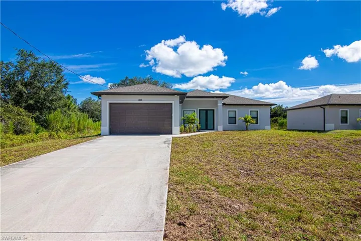Prairie-style home featuring an attached garage, concrete driveway, a front lawn, stucco siding, and roof with shingles