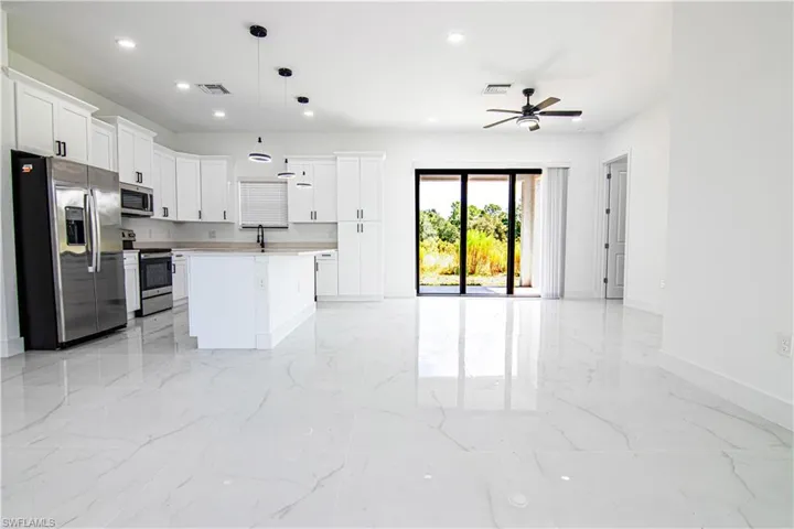 Kitchen with stainless steel appliances, white cabinetry, a kitchen island, open floor plan, and decorative light fixtures