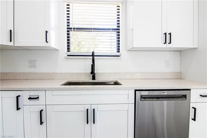 Kitchen with stainless steel dishwasher, white cabinetry, and light stone counters