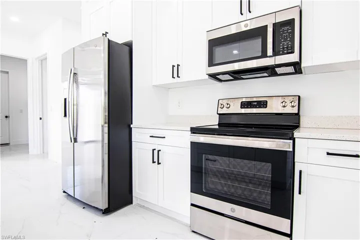 Kitchen featuring stainless steel appliances, light stone countertops, white cabinetry, light marble finish floors, and recessed lighting