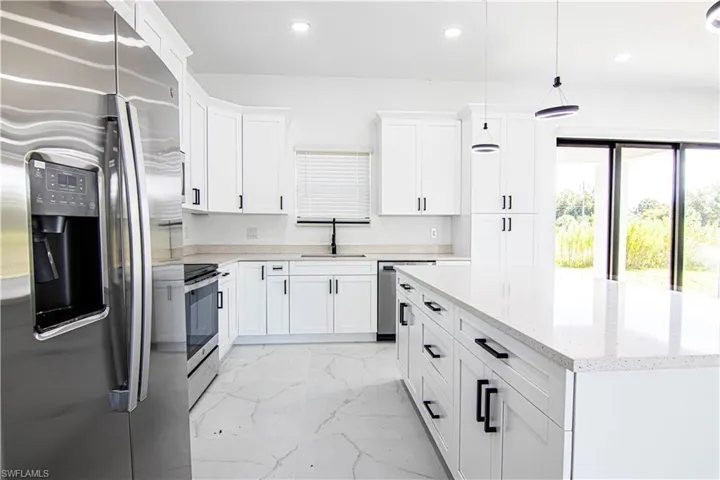 Kitchen featuring stainless steel appliances, white cabinets, pendant lighting, a kitchen island, and light marble finish flooring