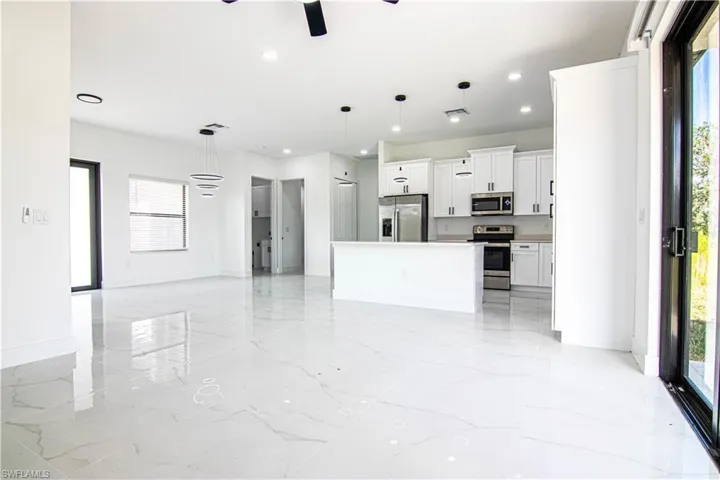 Kitchen with white cabinetry, open floor plan, hanging light fixtures, and stainless steel appliances