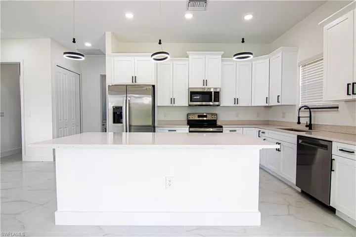 Kitchen with stainless steel appliances, a kitchen island, light stone counters, white cabinetry, and decorative light fixtures