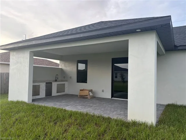 Back of property featuring area for grilling, sink, a lawn, and a patio