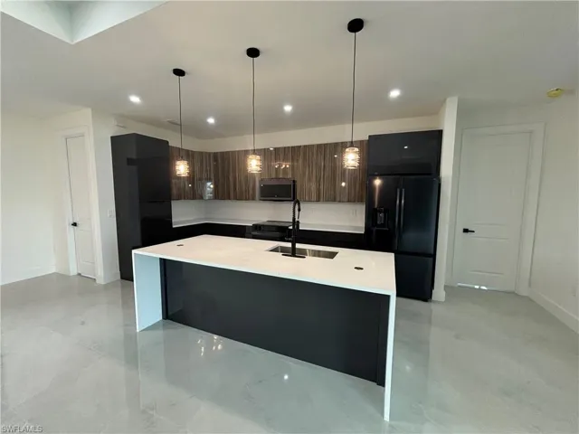 Kitchen with an island with sink, dark brown cabinets, decorative light fixtures, and black refrigerator with ice dispenser