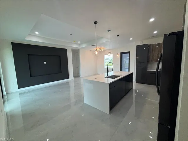 Kitchen with a tray ceiling, a kitchen island with sink, sink, decorative light fixtures, and black refrigerator