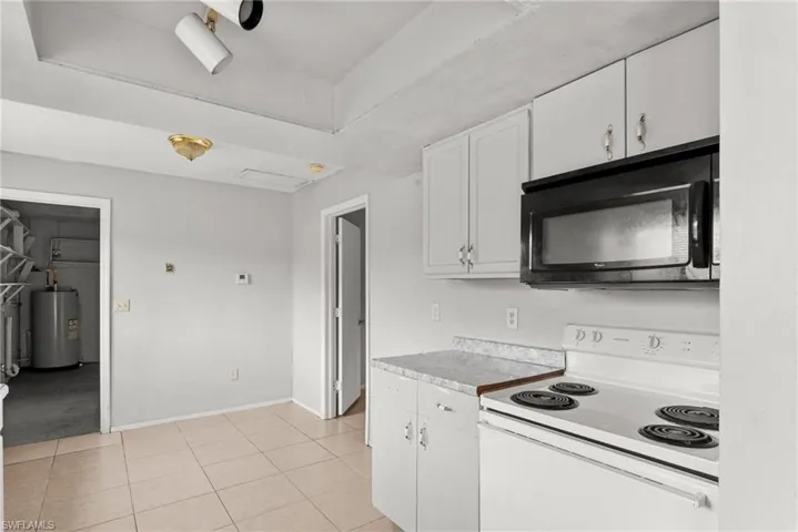 Kitchen with white range with electric cooktop, black microwave, white cabinets, light tile patterned floors, and electric water heater